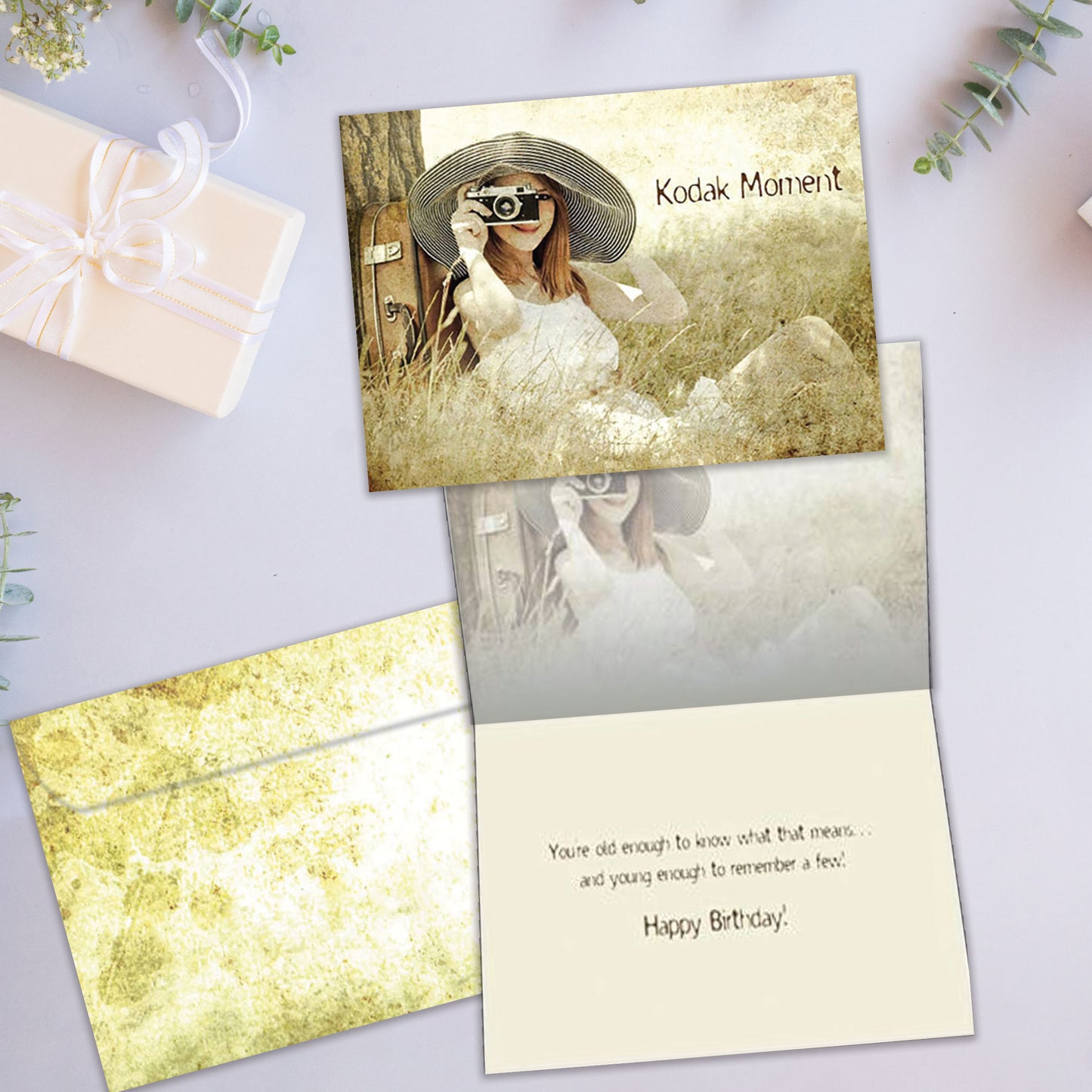 Front and inside view of a Birthday greeting card showcasing a woman sitting next to a tree taking a picture with the words "Kodak moment", with a matching envelope.