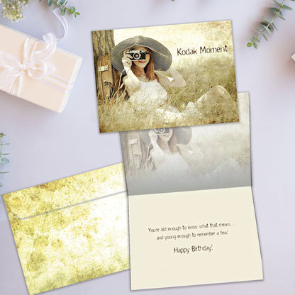 Front and inside view of a Birthday greeting card showcasing a woman sitting next to a tree taking a picture with the words "Kodak moment", with a matching envelope.