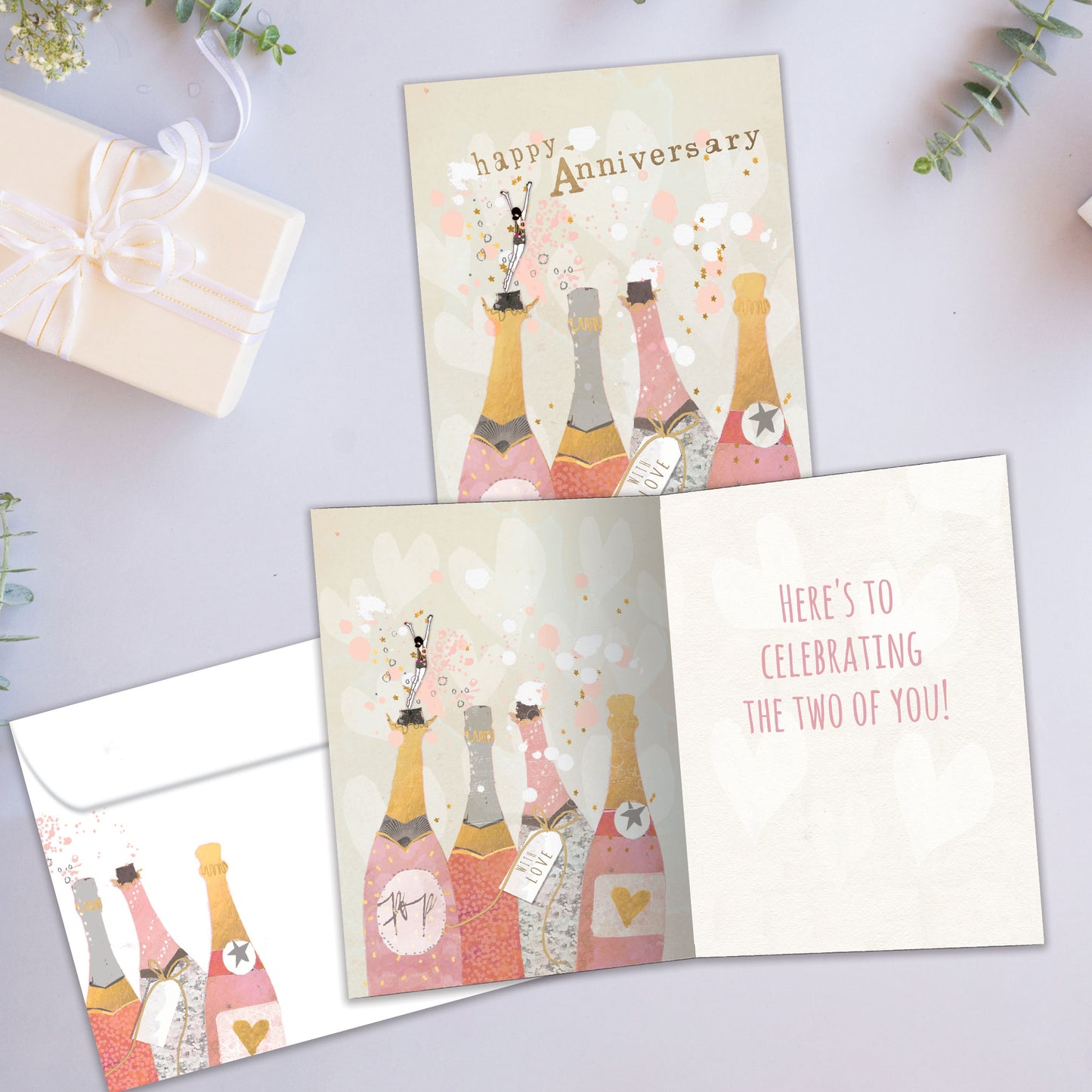 Front and inside view of an Anniversary greeting card showcasing champagne bottles with the words "Happy Anniversary," with a matching envelope.