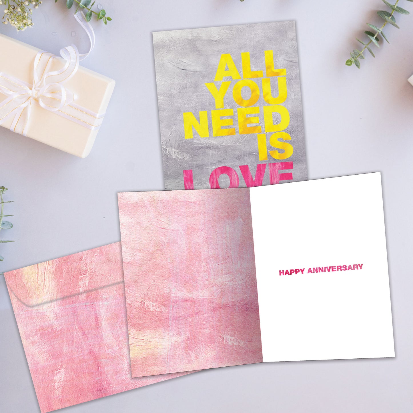 Front and inside view of an Anniversary greeting card showcasing the vibrant message "All you need is love," with a matching envelope.