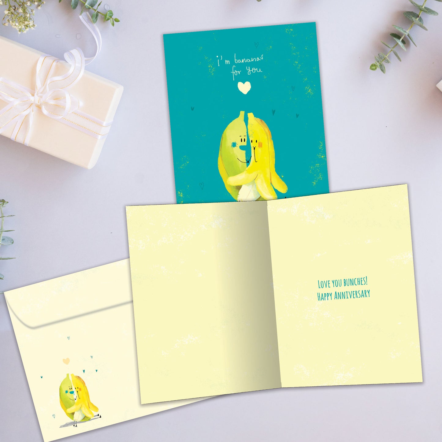 Front and inside view of an Anniversary greeting card showcasing two bananas hugging on a teal background with a loving message, with a matching envelope.