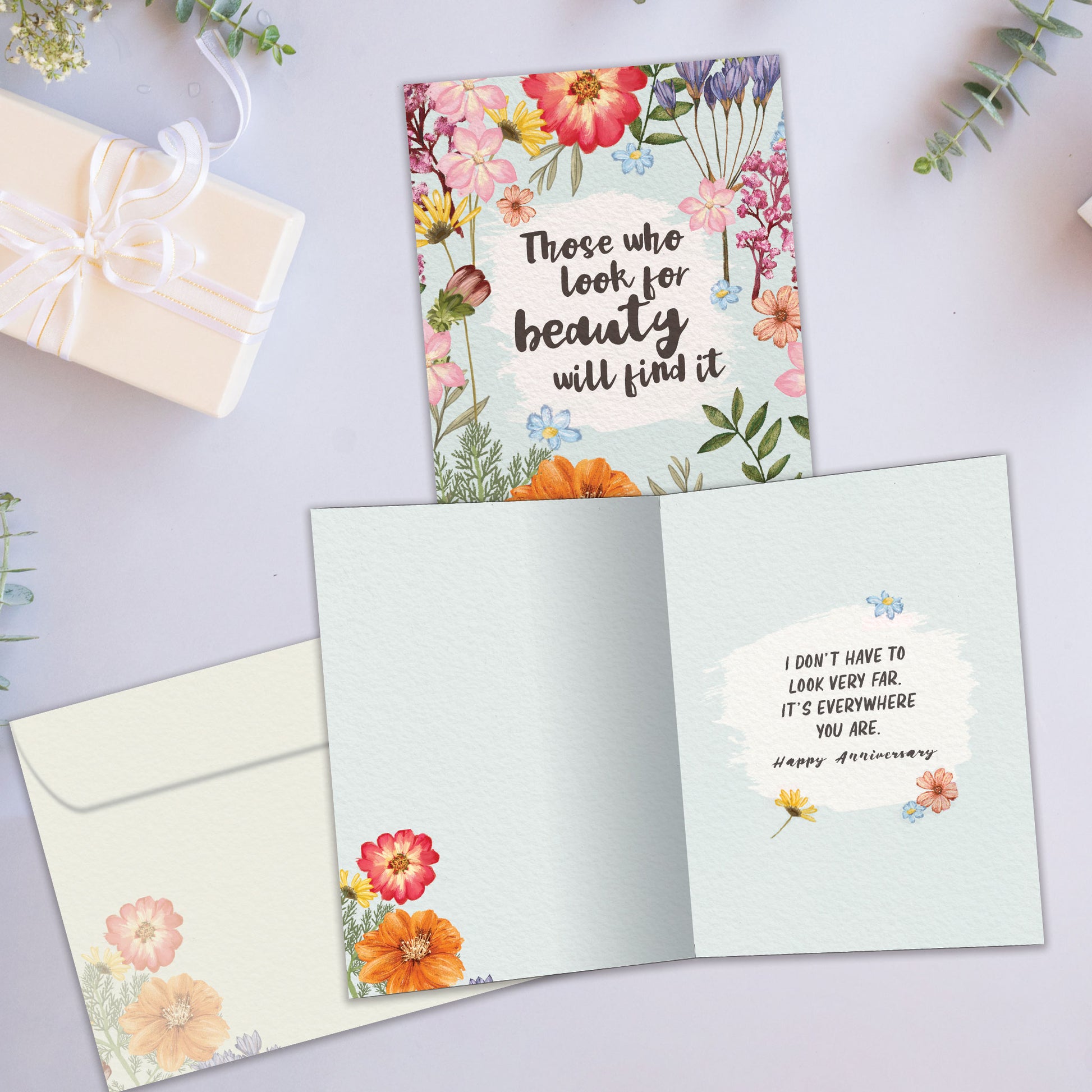 Front and inside view of an Anniversary greeting card showcasing a message about finding beauty with floral accents, with a matching envelope.