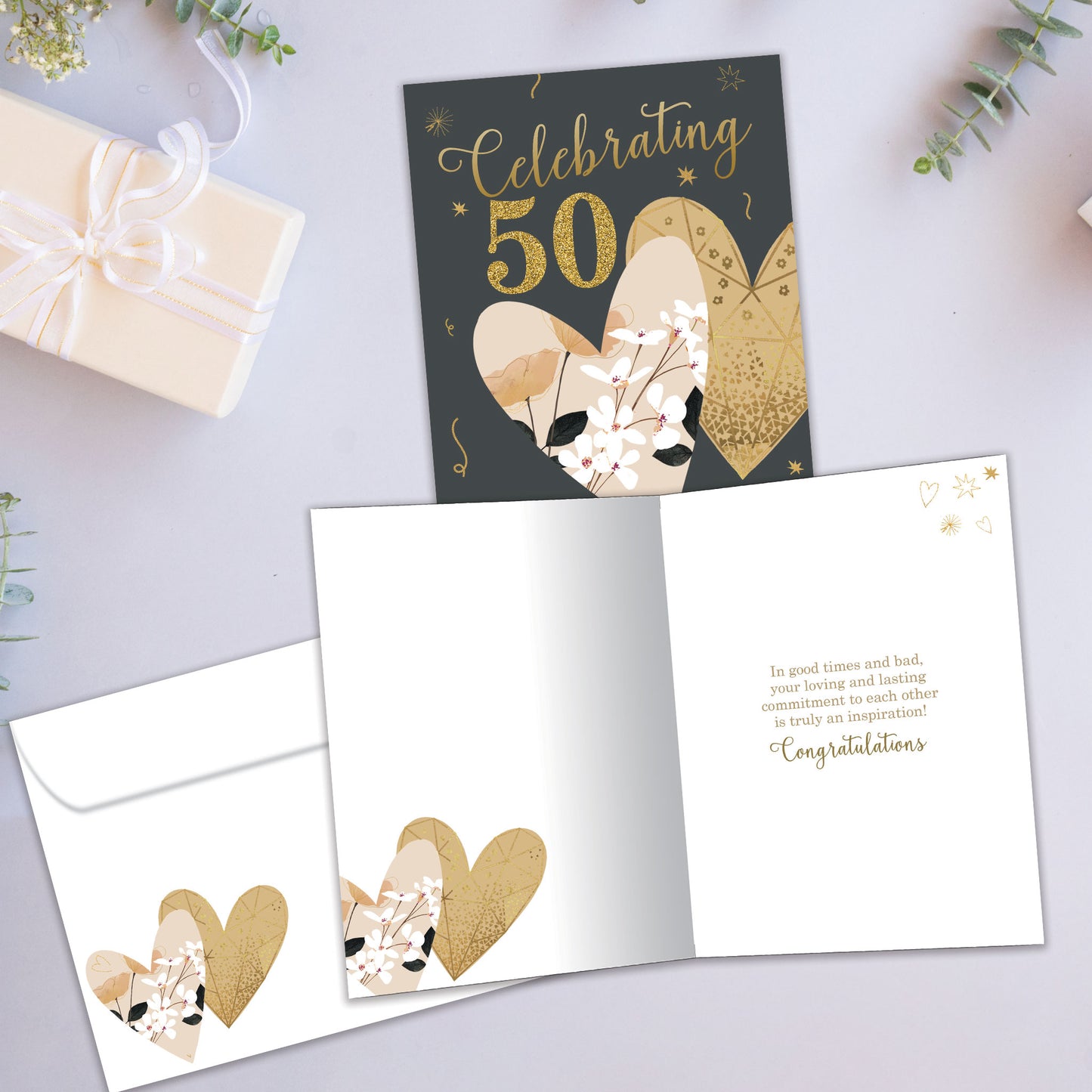 Front and inside view of an Anniversary greeting card showcasing "Celebrating 50 years" in gold on a dark background with two hearts, with a matching envelope.