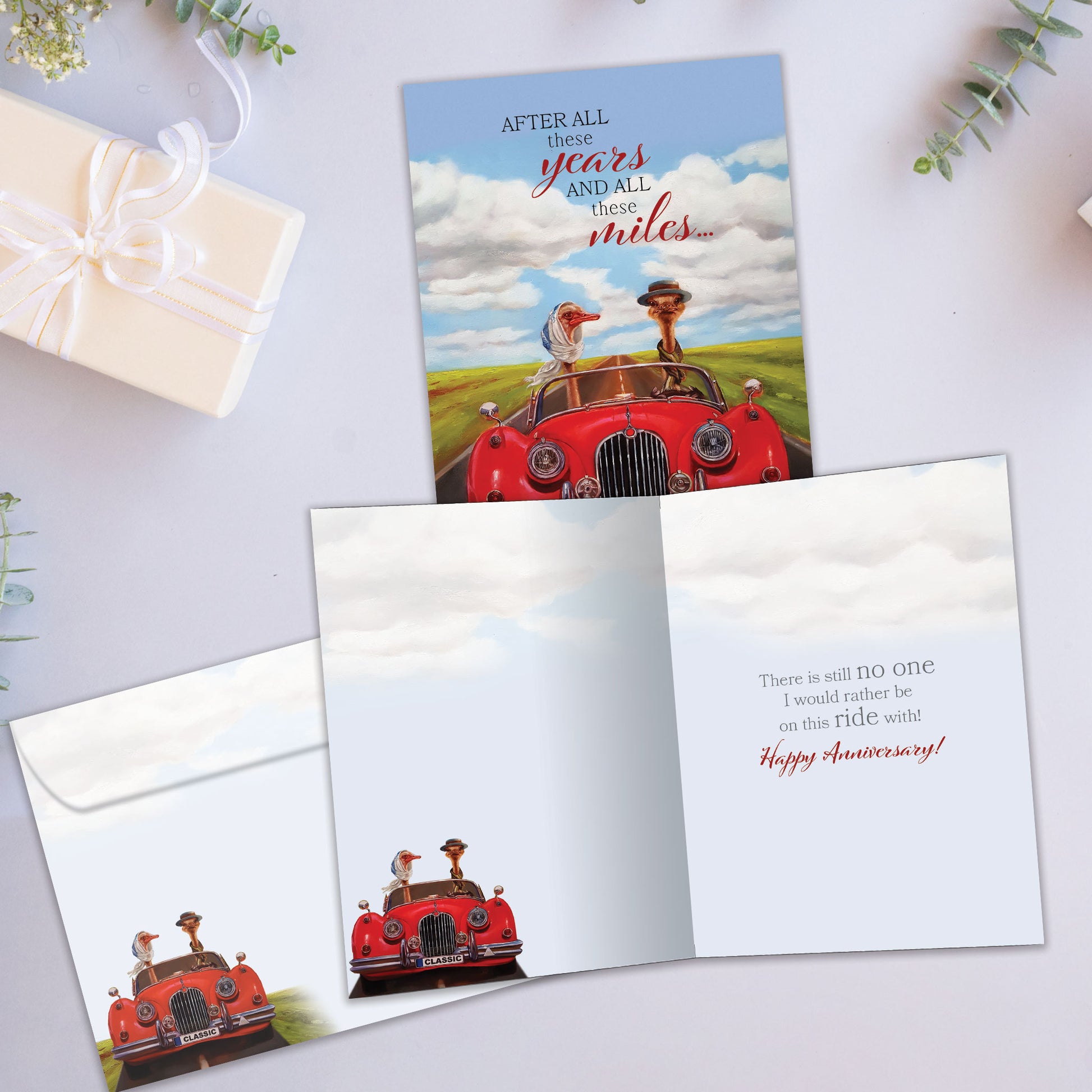 Front and inside view of an Anniversary greeting card showcasing a goose couple driving in a red car and a heartfelt message, with a matching envelope.
