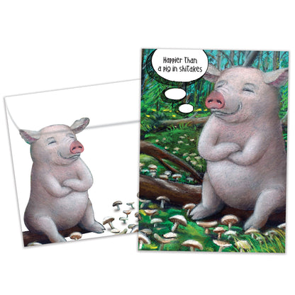 Front view of a Birthday greeting card and matching envelope featuring a happy pig sitting on a log with the message "Happier than a pig in shiitakes."