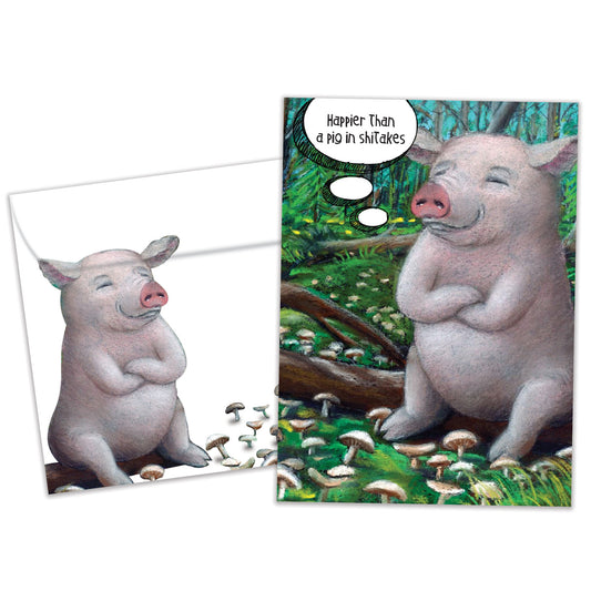 Front view of a Birthday greeting card and matching envelope featuring a happy pig sitting on a log with the message "Happier than a pig in shiitakes."