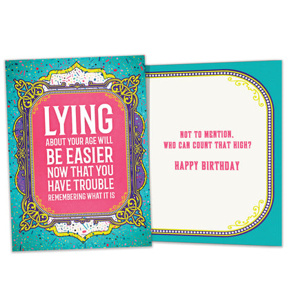 Front view of a Birthday greeting card featuring a funny message about lying about your age on a pink and teal background, with a matching envelope.