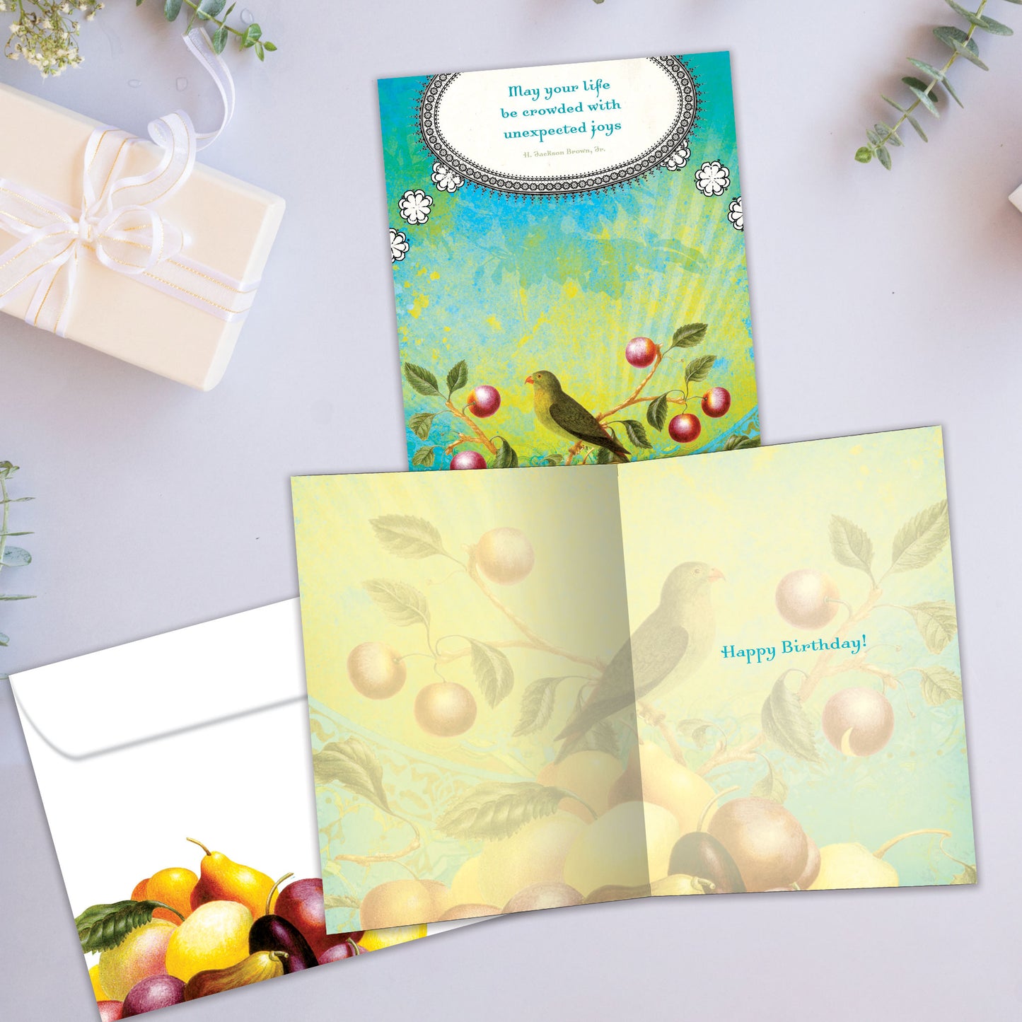 Front and inside view of a Birthday greeting card showcasing a joyful message alongside a bird and fruit illustration, complete with a matching envelope.