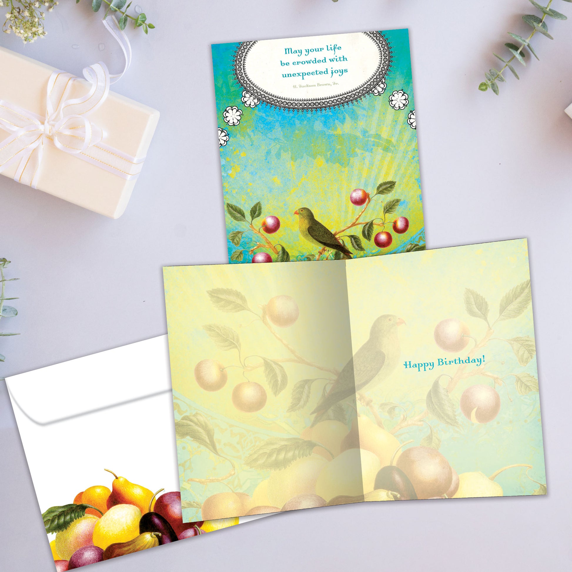Front and inside view of a Birthday greeting card showcasing a joyful message alongside a bird and fruit illustration, complete with a matching envelope.