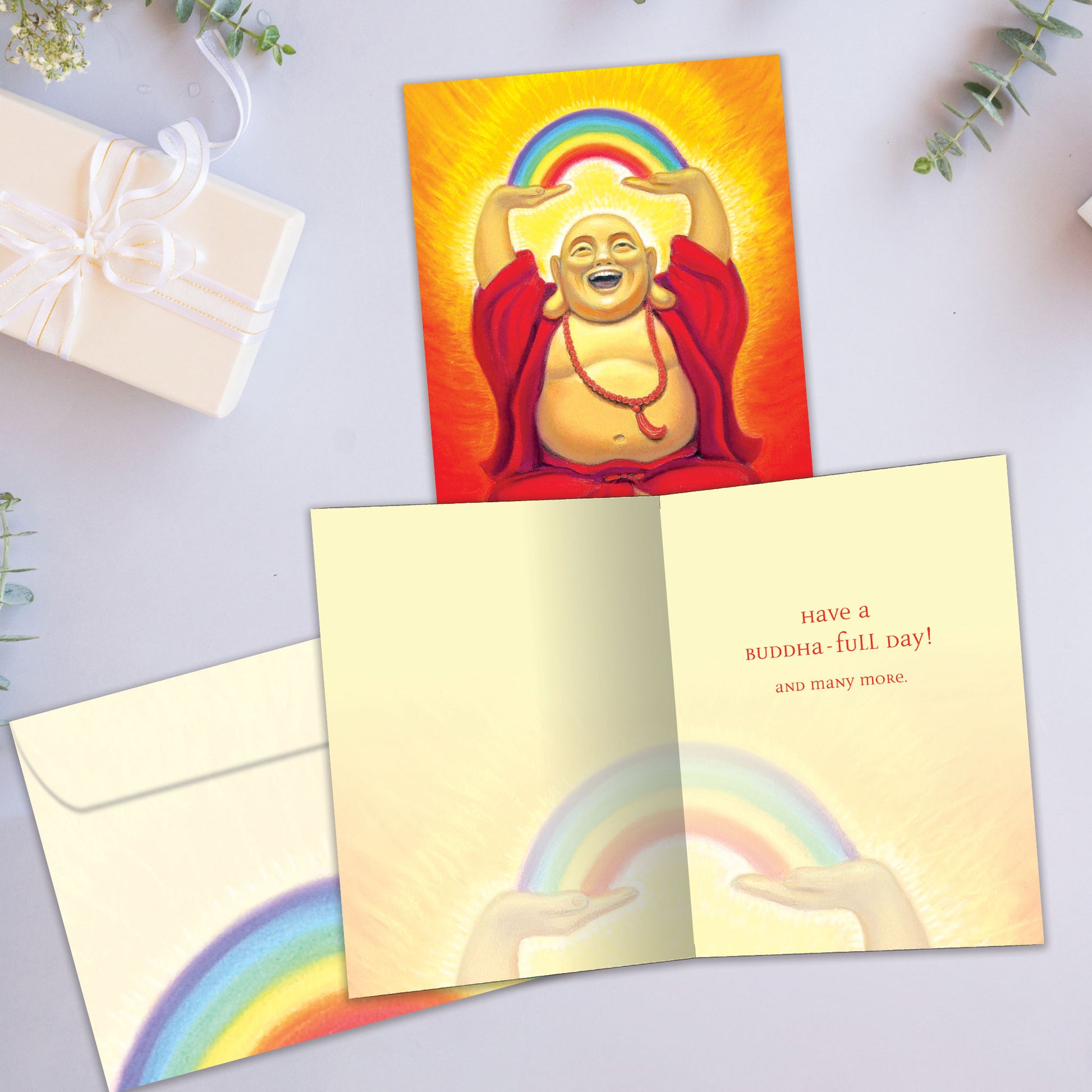 Front and inside view of a Birthday greeting card showcasing a laughing Buddha with a rainbow, accompanied by a matching envelope.