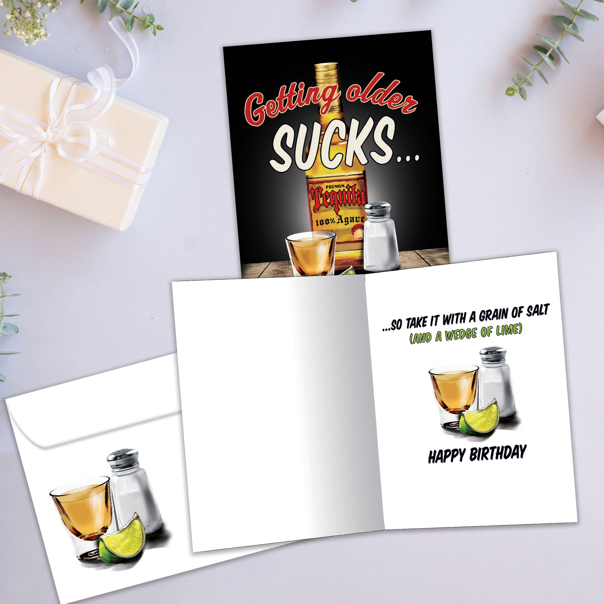 Front and inside view of a Birthday greeting card showcasing an illustration of tequila and salt with the message "getting older sucks," with a matching envelope.