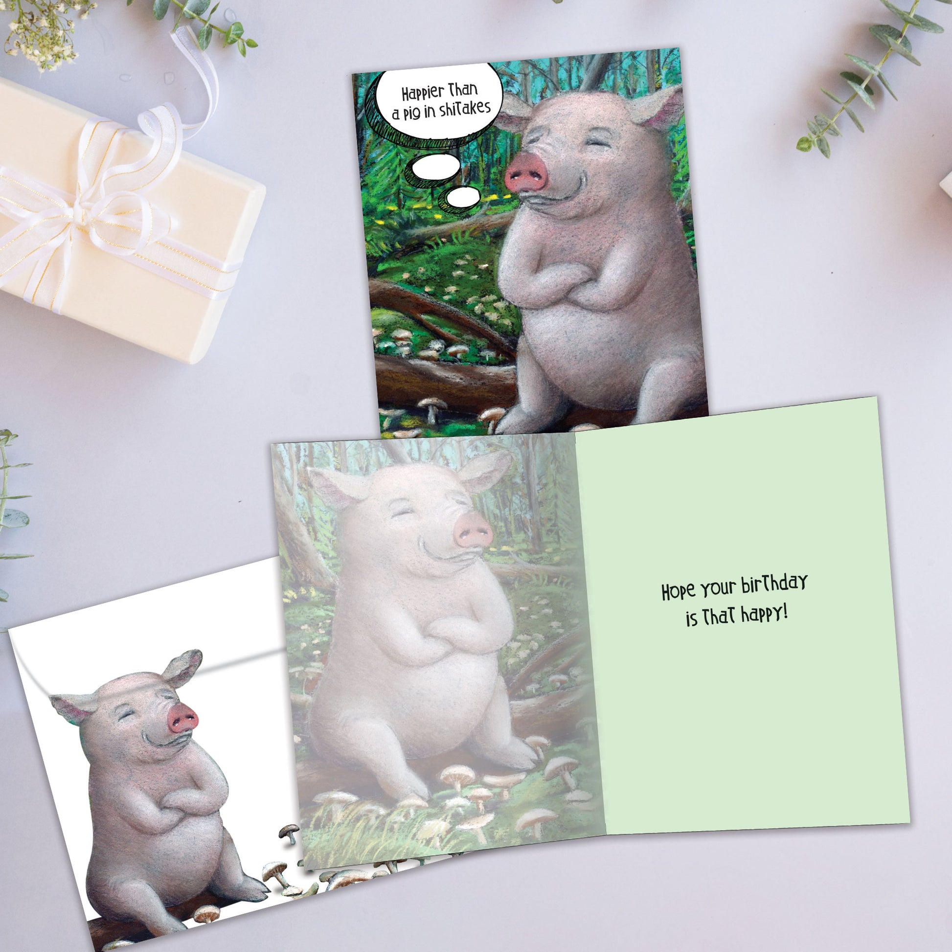 Front and inside view of a Birthday greeting card showcasing a joyful pig on a log with "Happier than a pig in shiitakes" and a matching envelope.