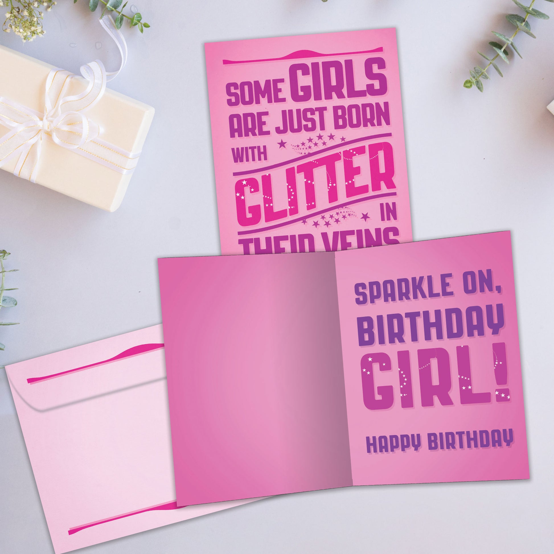 Front and inside view of a Birthday greeting card showcasing a cheerful message about girls born with glitter on a pink background, with a matching envelope.