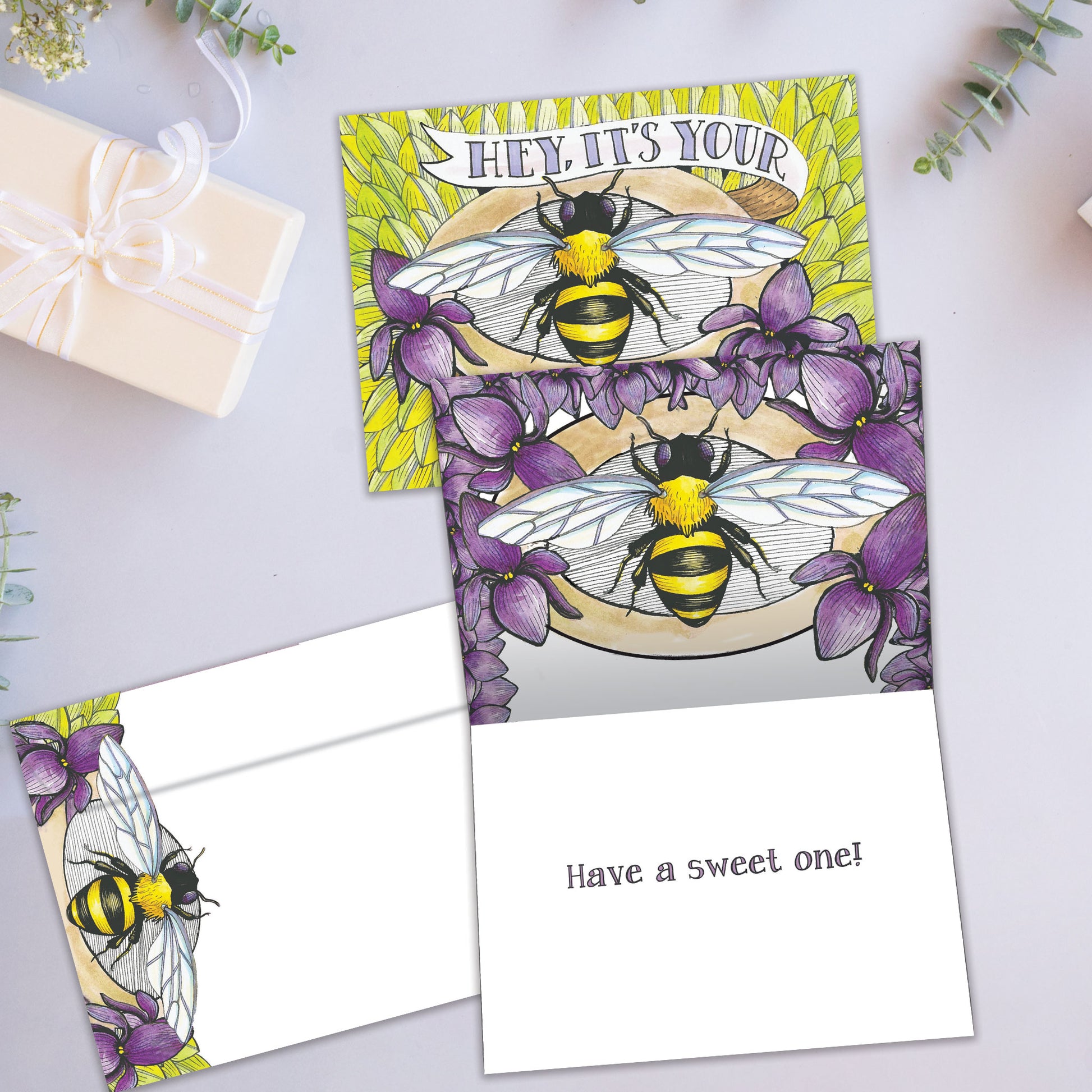 Front and inside view of a Birthday greeting card showcasing the message "Hey, it's your bee-day" with a bee and flowers, with a matching envelope.