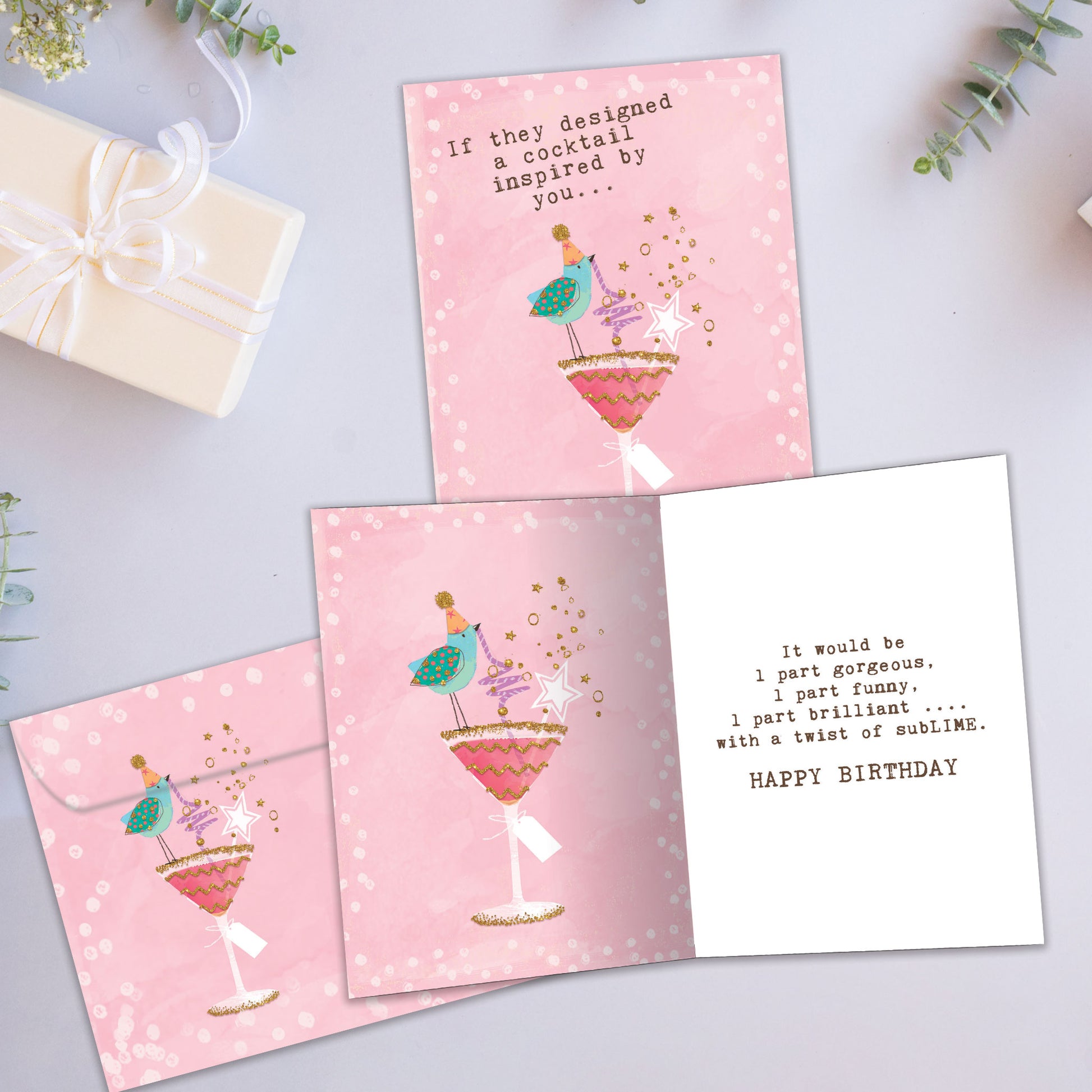 Front and inside view of a Birthday greeting card showcasing a bird sipping a cocktail with a pink background, with a matching envelope.